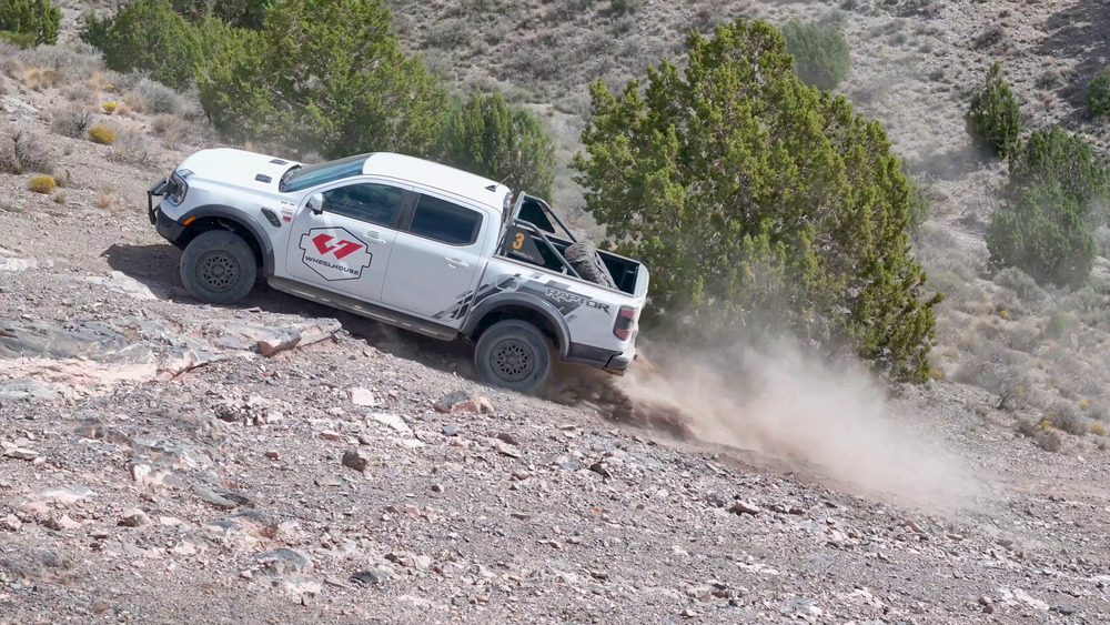 Five Mile Pass'te kayalık bir yamaca tırmanan, arka tekerleklerinin ardında toz bulutu yükselen beyaz Ford Ranger Raptor