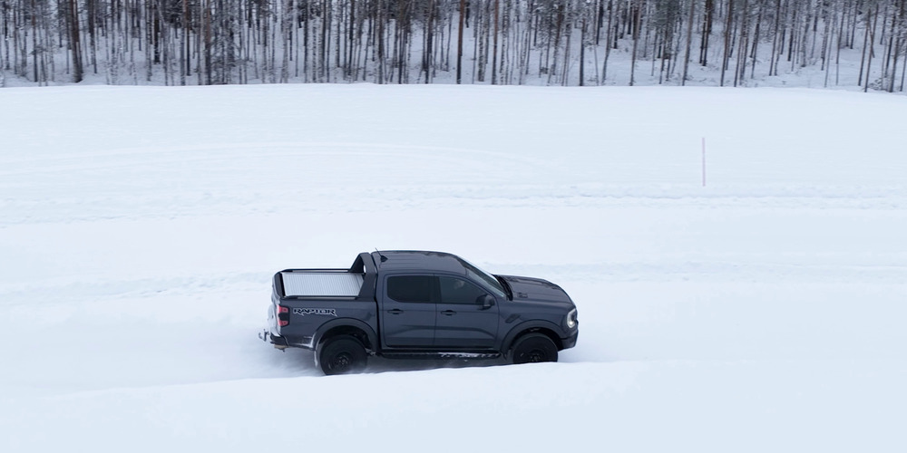 Orman kenarında karla kaplı bir test parkurunda ilerleyen gri Ford Ranger Raptor